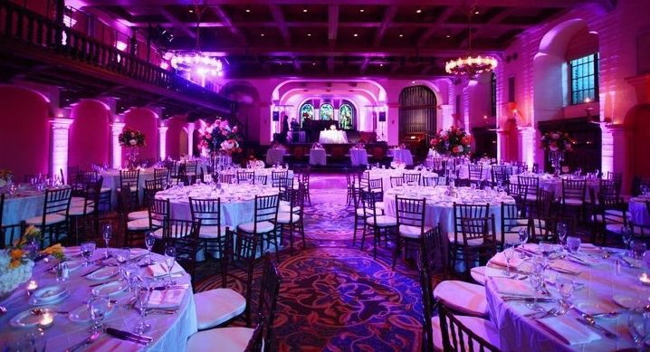 A ballroom set for dinner, lit wall-to-wall in magenta LED up-lighting.
