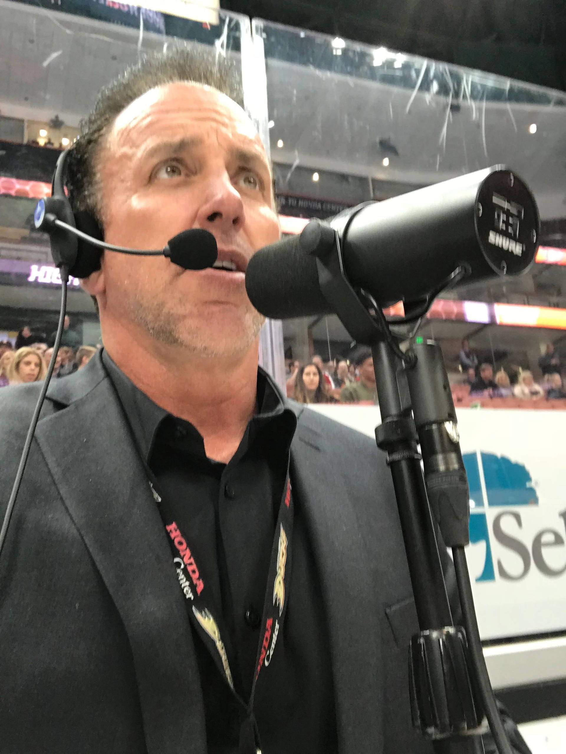 Devin Christopher rink-side in a headset, announcing at an Anaheim Ducks game.